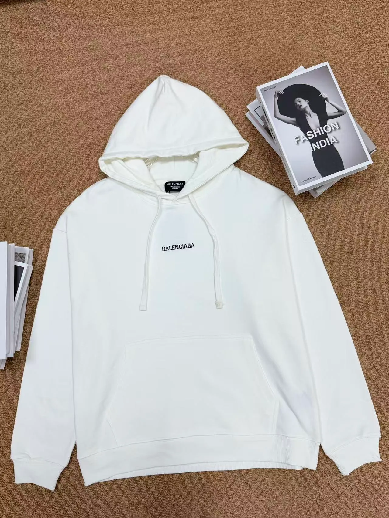 No. 2208 Style: Balenciaga Retro lettered hooded sweatshirt Color: Black, Cream White Version: Oversize loose shoulder, Same style for men and women, lazy and relaxed, covering the flesh and making you look slim Fabric: 430g high gram weight pure cotton terry fabric, soft and thick, with good drape, the upper body is not easy to wrinkle. Design highlights 1. White model: The small logo on the chest is simple and clean, minimalist and low-key style, and the daily Versatile is not picky. 2. Black model: Multi-layered Retro letter printing on the back, white rose red contrasting colors, strong layering, full of trendy atmosphere, the back printing is the visual focus of the entire dress. 3. Classic kangaroo pocket + adjustable drawstring brim, threaded cuffs and hem, Wear-Resistant is not easy to deform, and the workmanship is neatly routed. Wearing scenarios: Suitable for daily outings, commuting, and casual outings. Black is cool and stylish, and looks trendy when paired with jeans, wide-leg pants, and overalls; White is refreshing and simple, suitable for gentle casual style, and can also be worn as a couple's style. Washing and care tips: Machine wash/hand wash with cold water on the reverse side, do not rub the printed area vigorously, and dry in a cool place to avoid exposure to the sun, which may cause the print to crack and fade.
